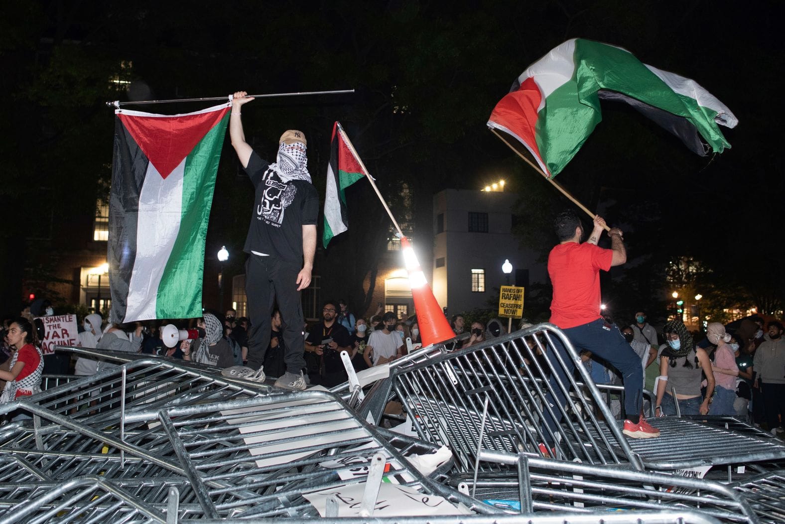 People waiving Palestinians flags on top of a pile of barriers, with a crowd in the background.