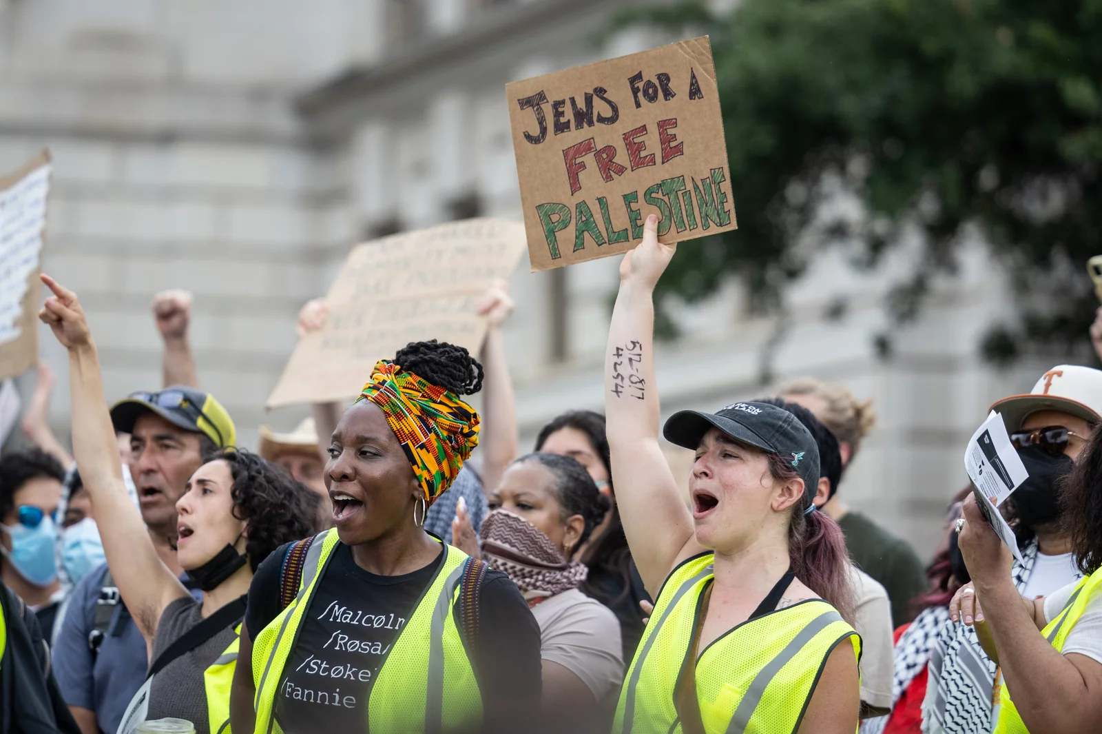 Protestors wearing yellow vests chanting, with one holding a sign saying "Jews for a Free Palestine"