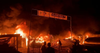 Incendie massif avec fumée noire remplissant le ciel et une bannière avec des caractères arabes et un drapeau palestinien.