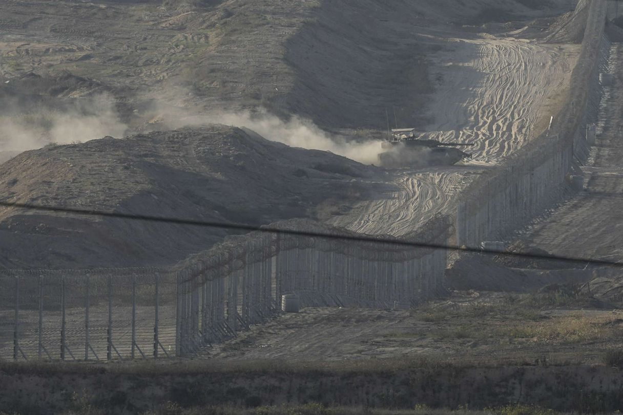 An Israeli tank manoeuvres in sandy fields, near a fence with barbed wire