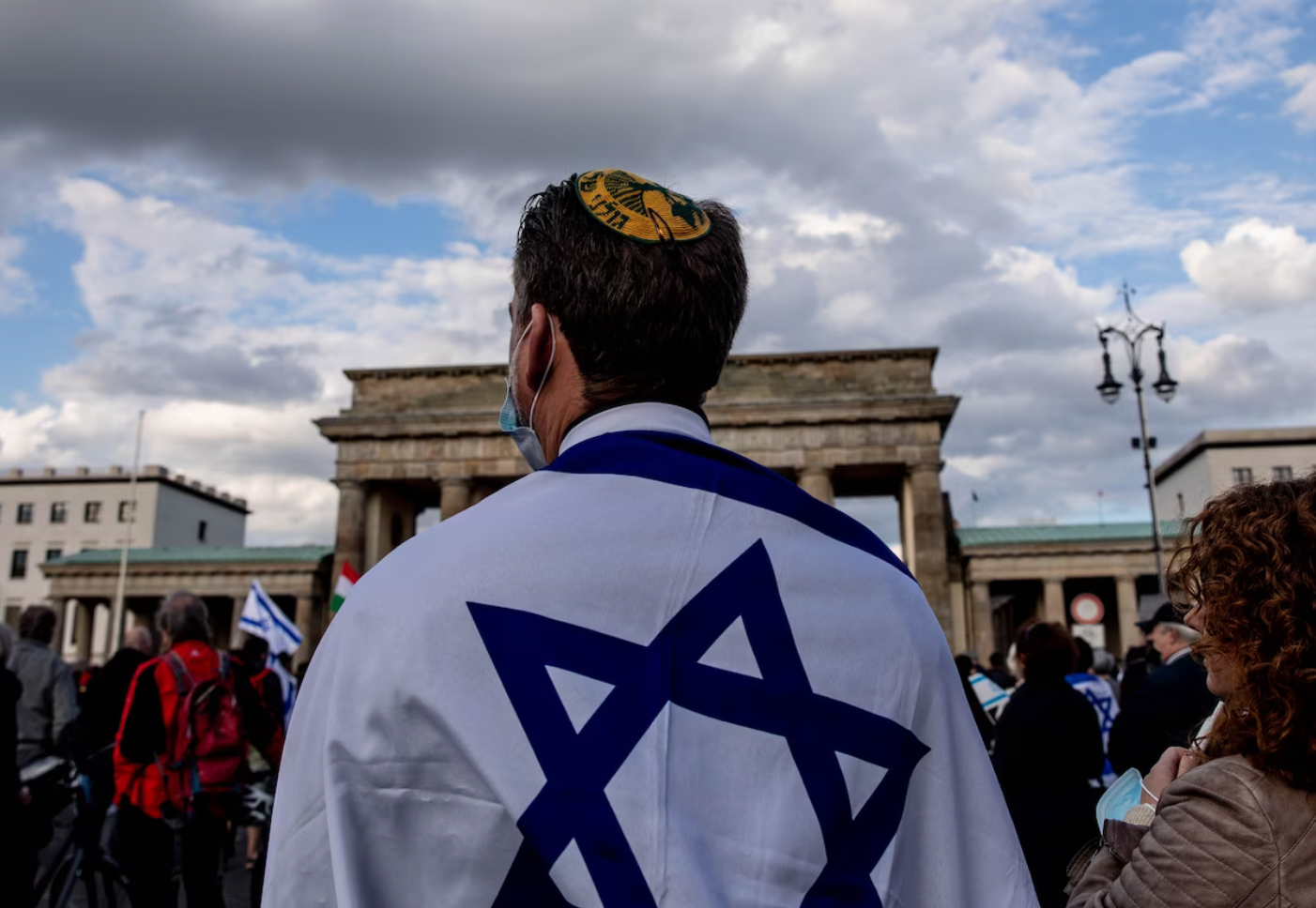 A person with a kippa and an Israeli flag on their back stands in a crowd where we can see a few Israeli flags