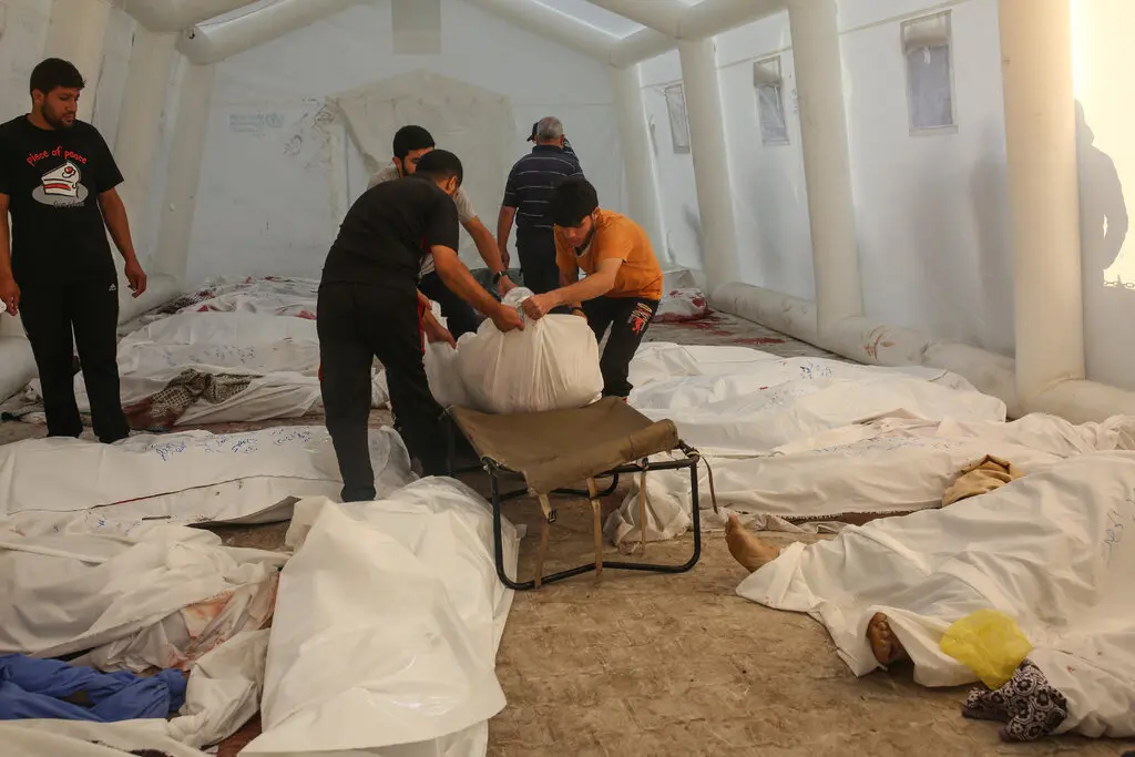 Men move bodies draped in white sheets in a white tent.