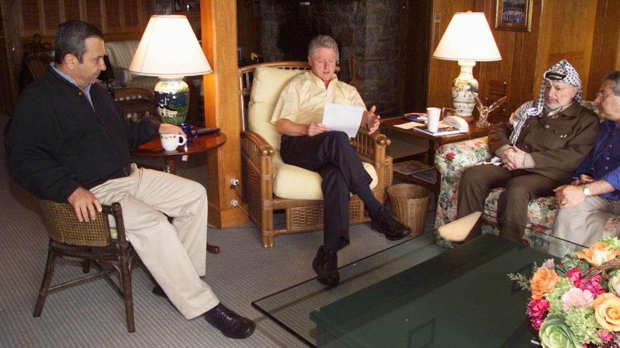 Ehud Barak, Bill Clinton, et Yasser Arafat assis dans un salon, avec Bill Clinton qui lit un document.